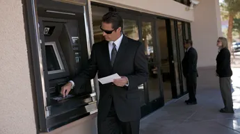Man using an ATM while holding a financial document, representing transactions that may be examined in a Nevada forgery investigation.