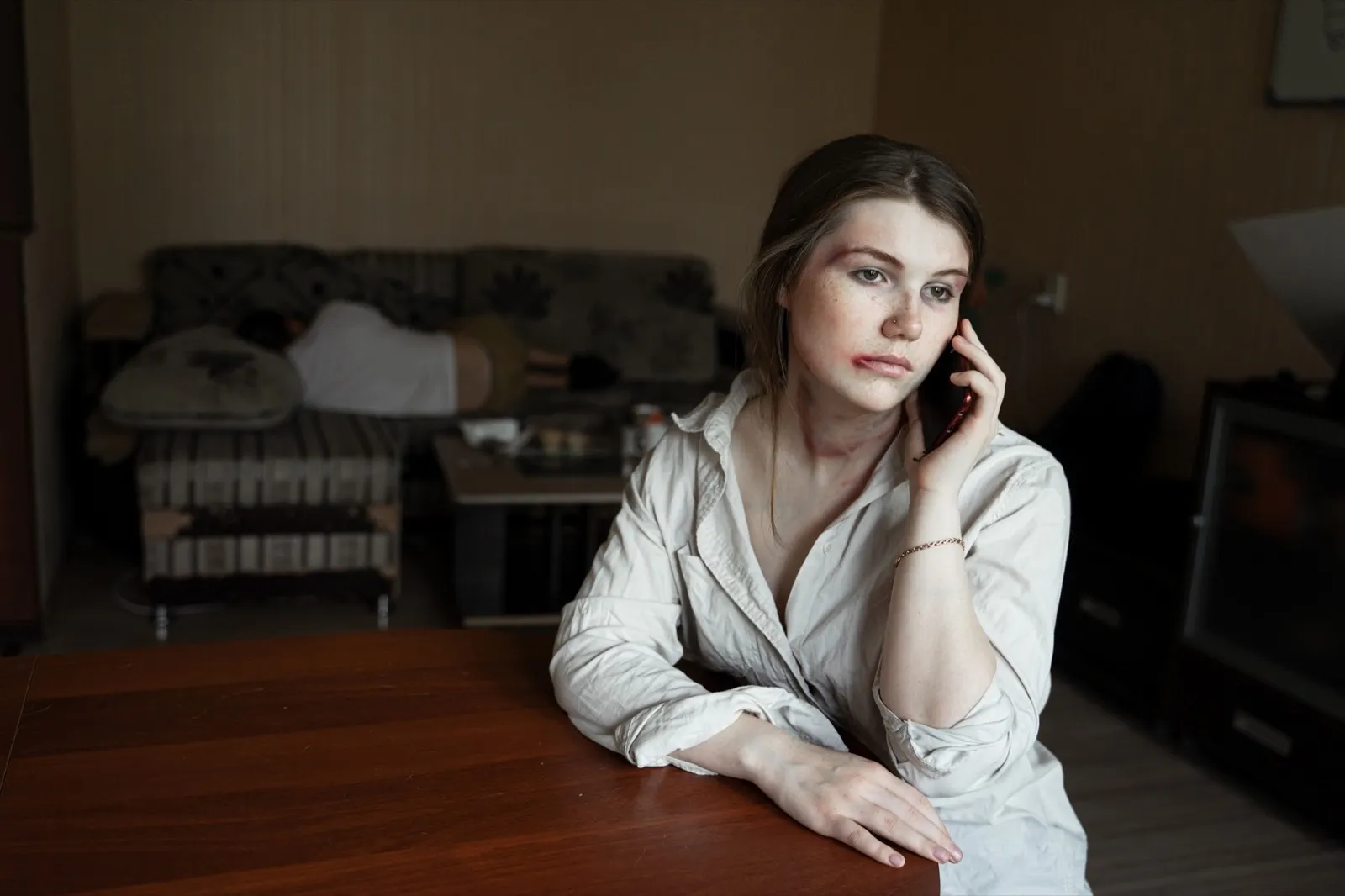 a girl who suffered from domestic violence sits at a table with a phone in her hands