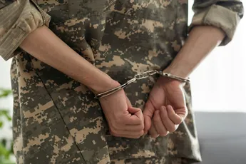 A handcuffed soldier behind the bars against a black background. Concept: court martial, refusal to