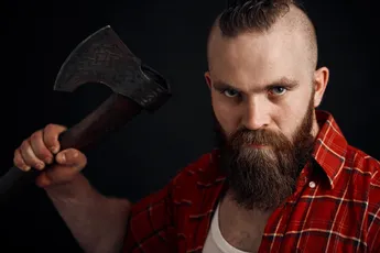 agressive lumberjack. bearded man swinging with axe