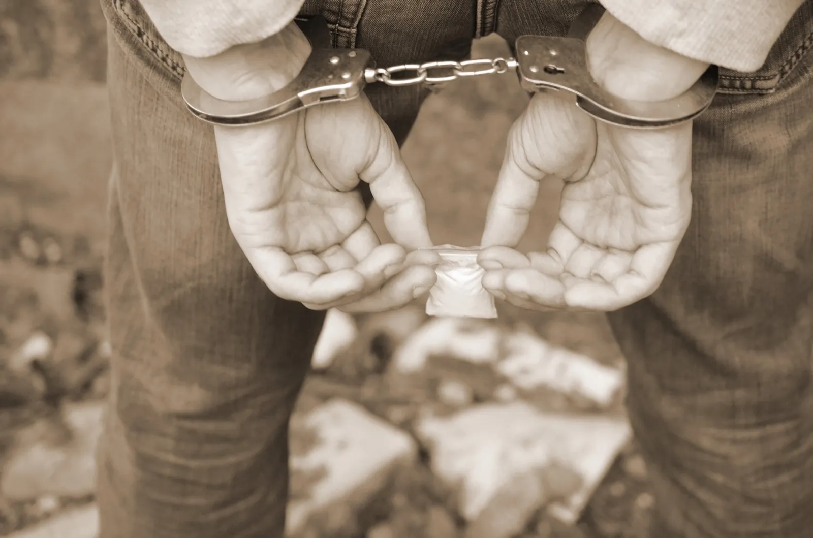 Arrested drug dealer in police handcuffs with small heroin drug