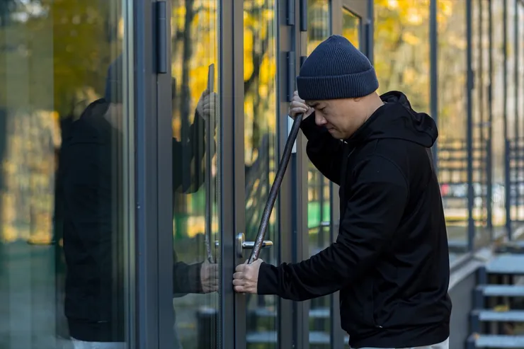 Asian man robber tries to break the door lock with a large metal crowbar tool