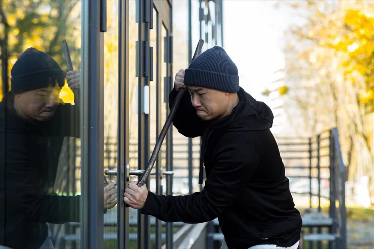 Asian man robber tries to break the door lock with a large metal crowbar tool
