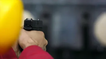 Back view of man shoots a gun at shooting range close up. Man fires hand gun at indoor shooting