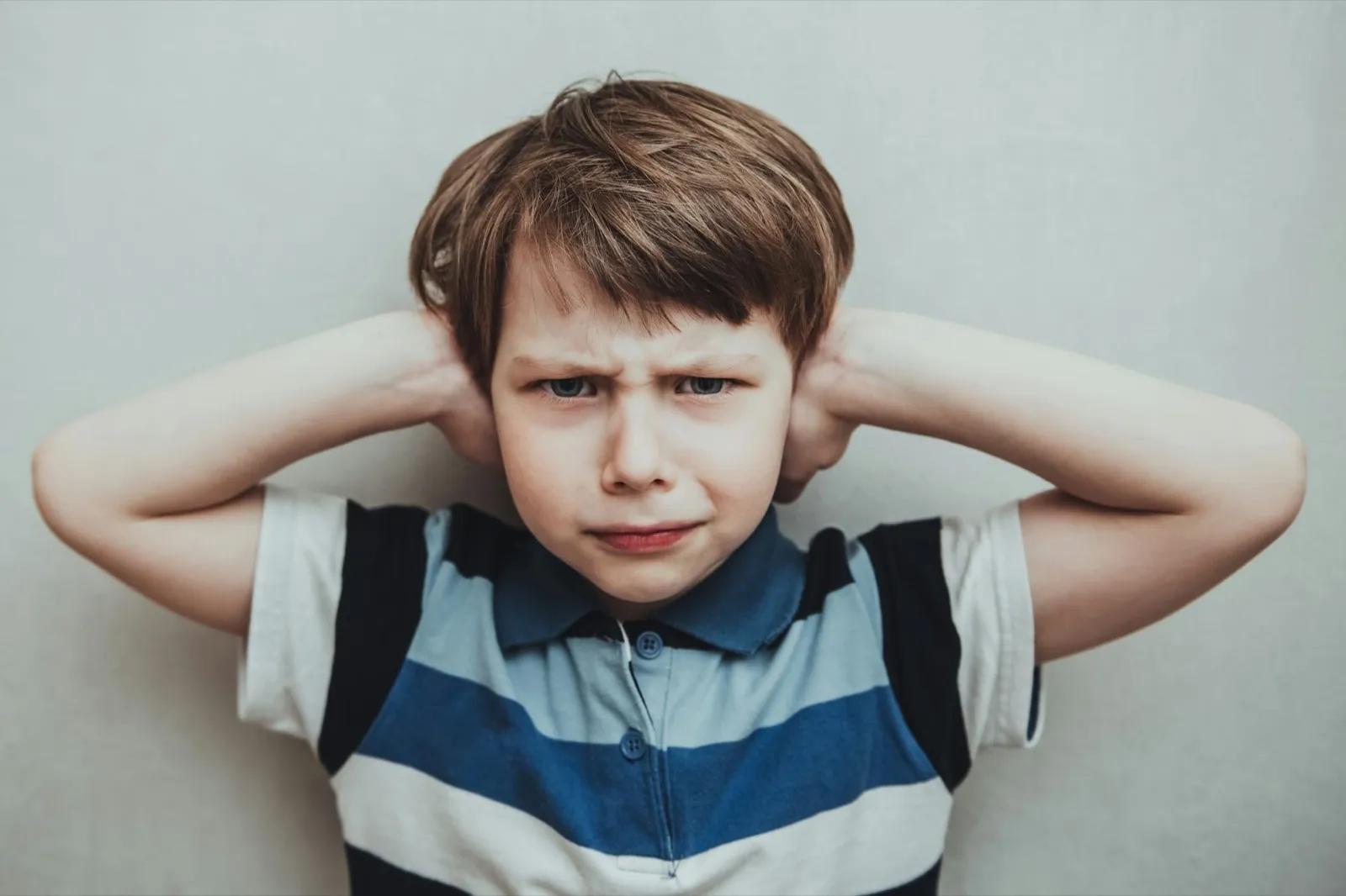 Child boy against gray background covering ears with hands. Domestic violence