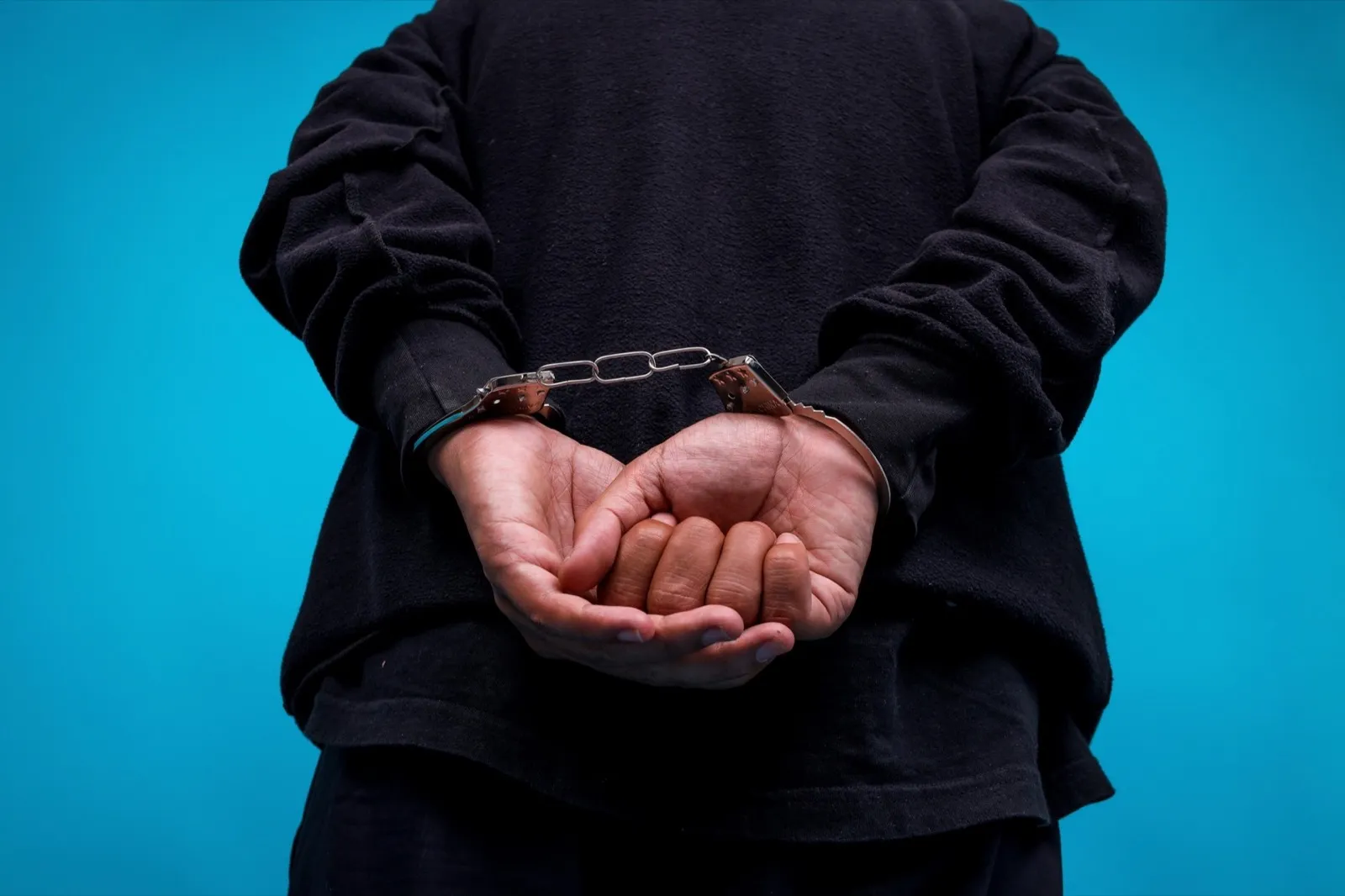 Close-up Of Hands Arrested With Handcuffed In Back Isolated On Blue Background