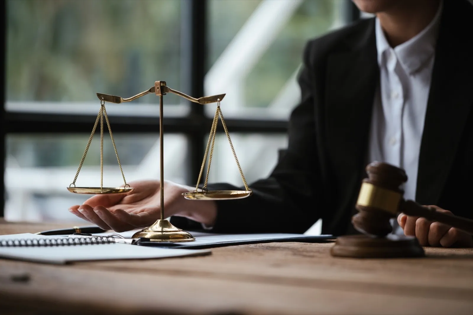 Close up of lawyer’s hands and scale of justice on table in the office.