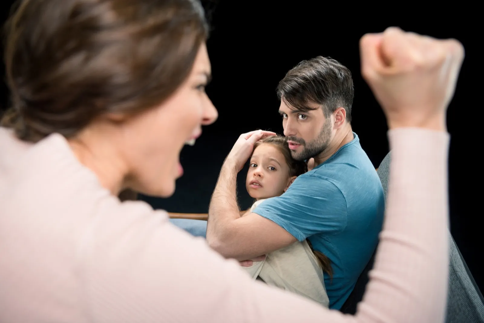 father protecting daughter from aggressive mother isolated on black, family violence concept