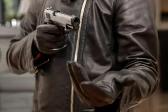 Gloved hand holding a pistol aiming, closeup view. Armed robbery concept