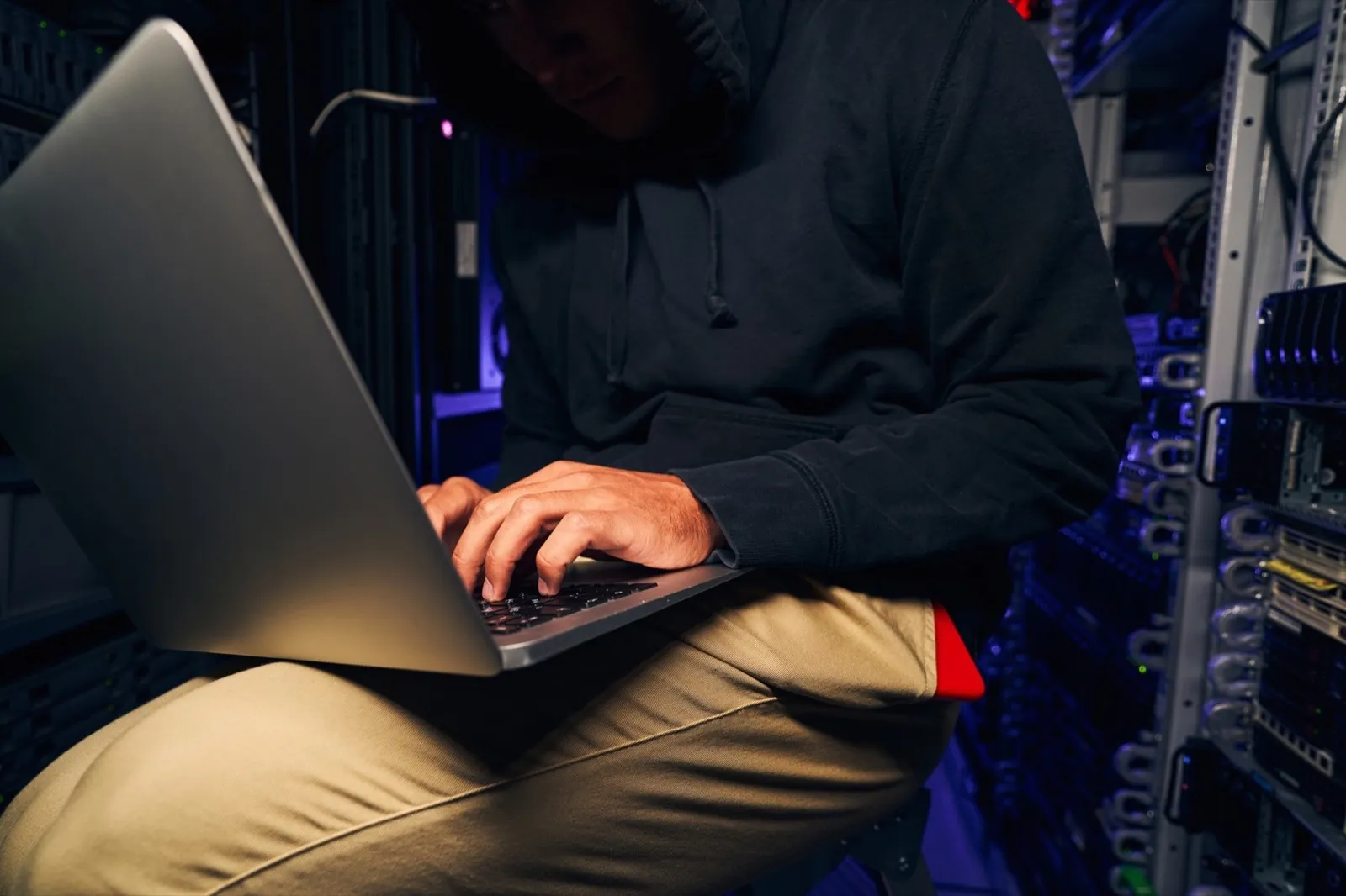 Hacker typing on his laptop in dark server room