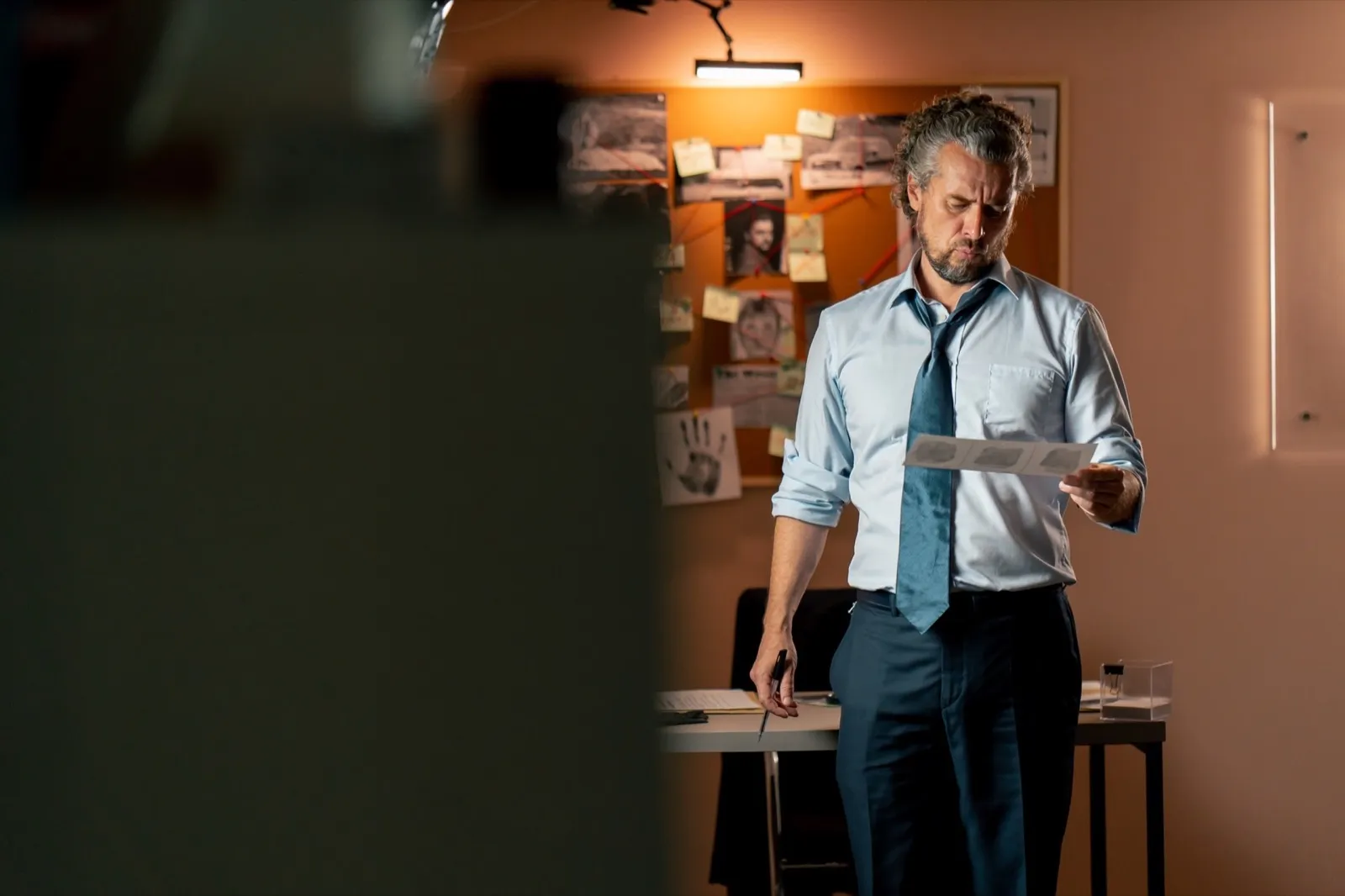 in the detective’s office middle-aged investigator in a shirt and tie examines with a magnifying