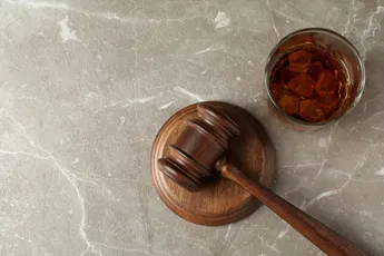 Judge gavel and glass of whiskey on gray textured table