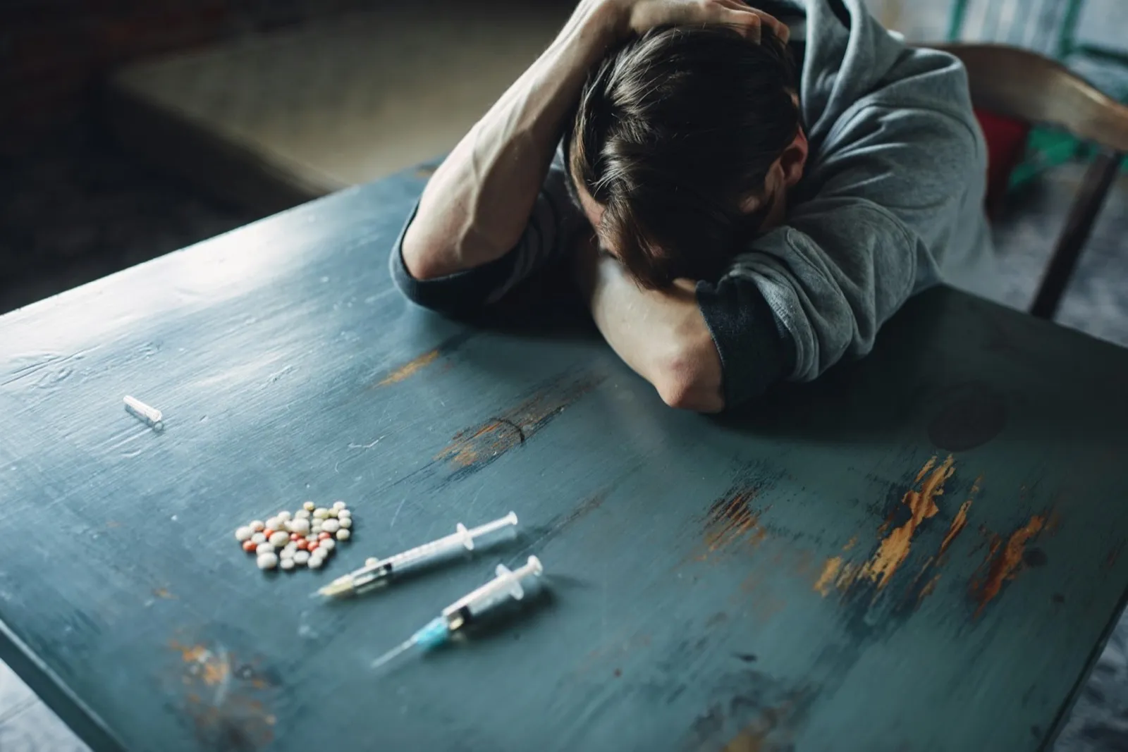 Male junkie at the table with drugs and syringe