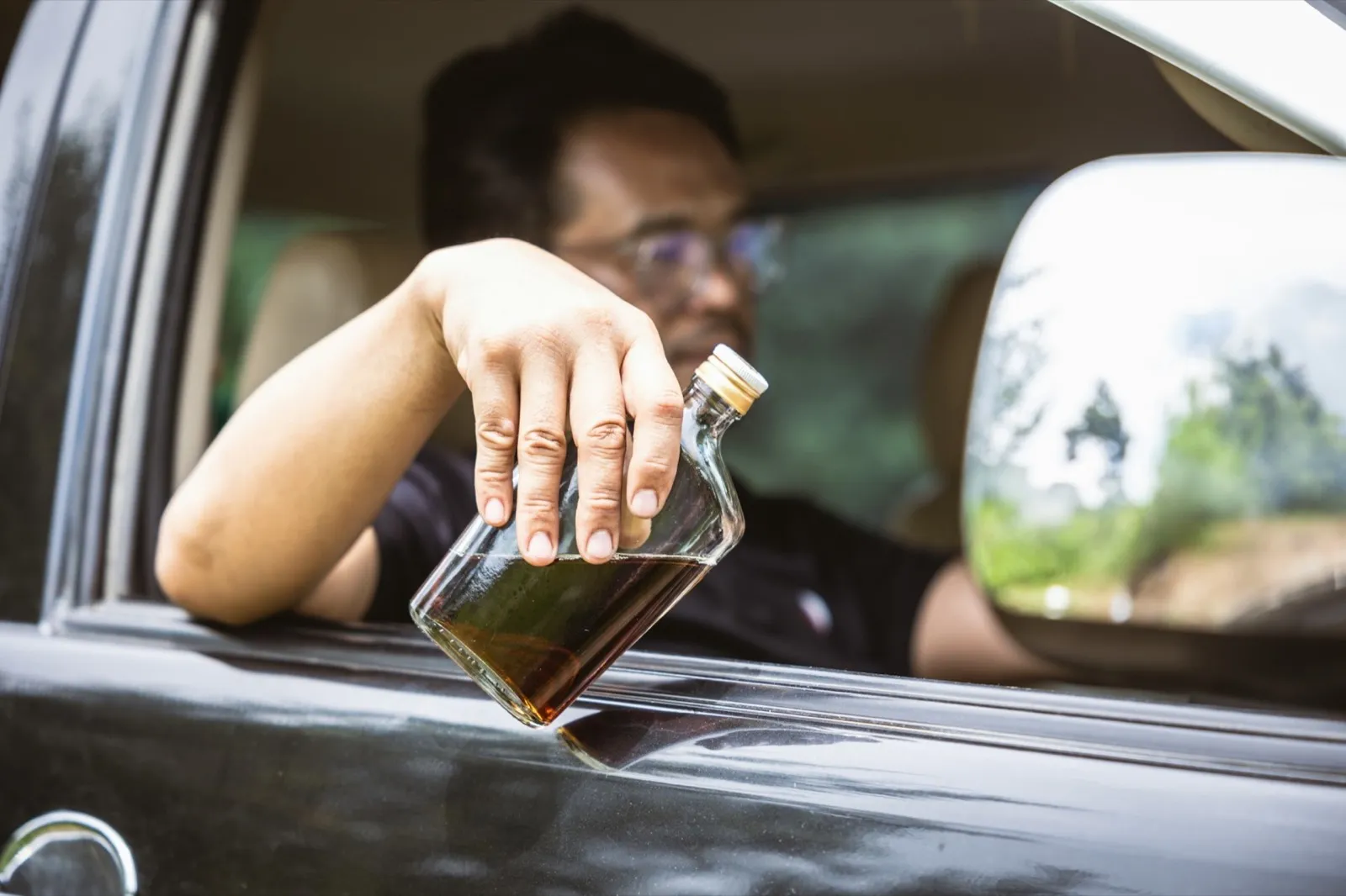 man drunk during drive a car. driver with alcohol whisky bottle dangerous and illegal concept.
