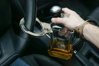 Man in handcuffs holds bottle of alcohol in car. Drunk driving concept. Don't drink and drive.