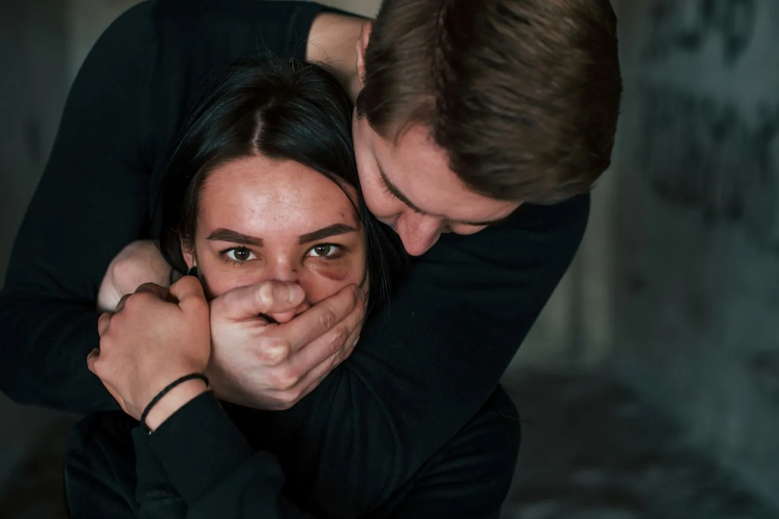 Man’s hand covering her mouth. Kidnapped woman is threatened by guy