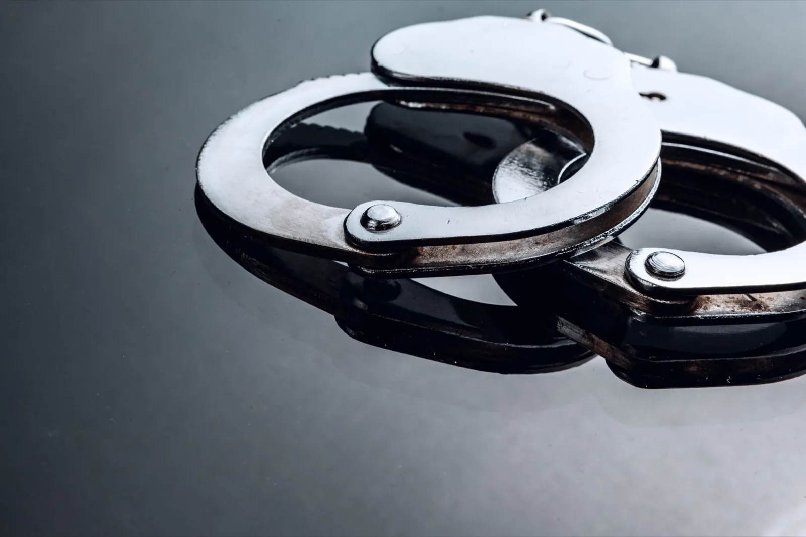 Metal closed handcuffs on black background with reflection