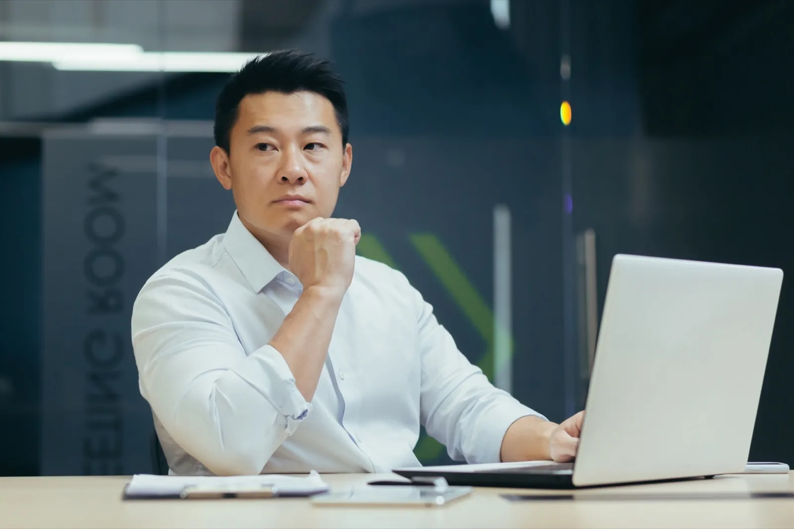 Portrait of a young Asian lawyer. He sits seriously in the office at the desk with a laptop