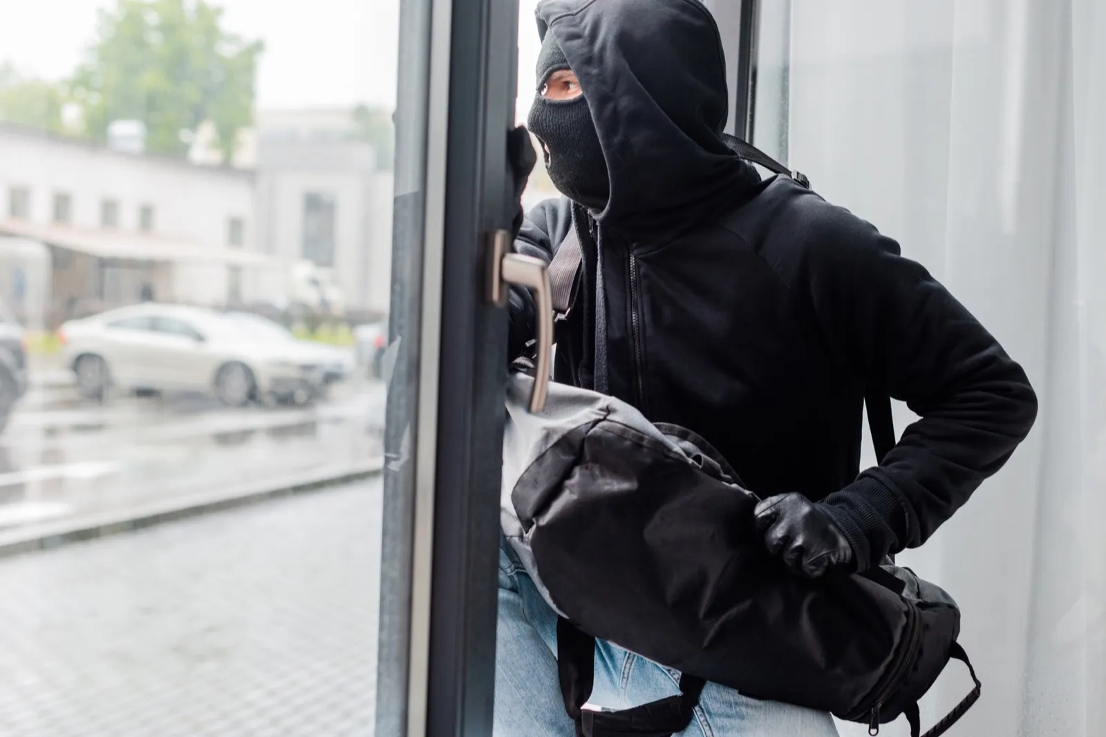 Robber in balaclava and leather gloves holding bag near open window