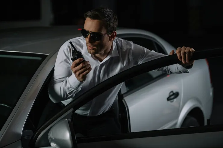 serious male undercover agent in sunglasses using talkie walkie near car