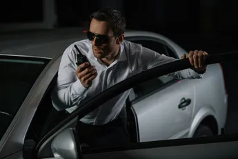 serious male undercover agent in sunglasses using talkie walkie near car