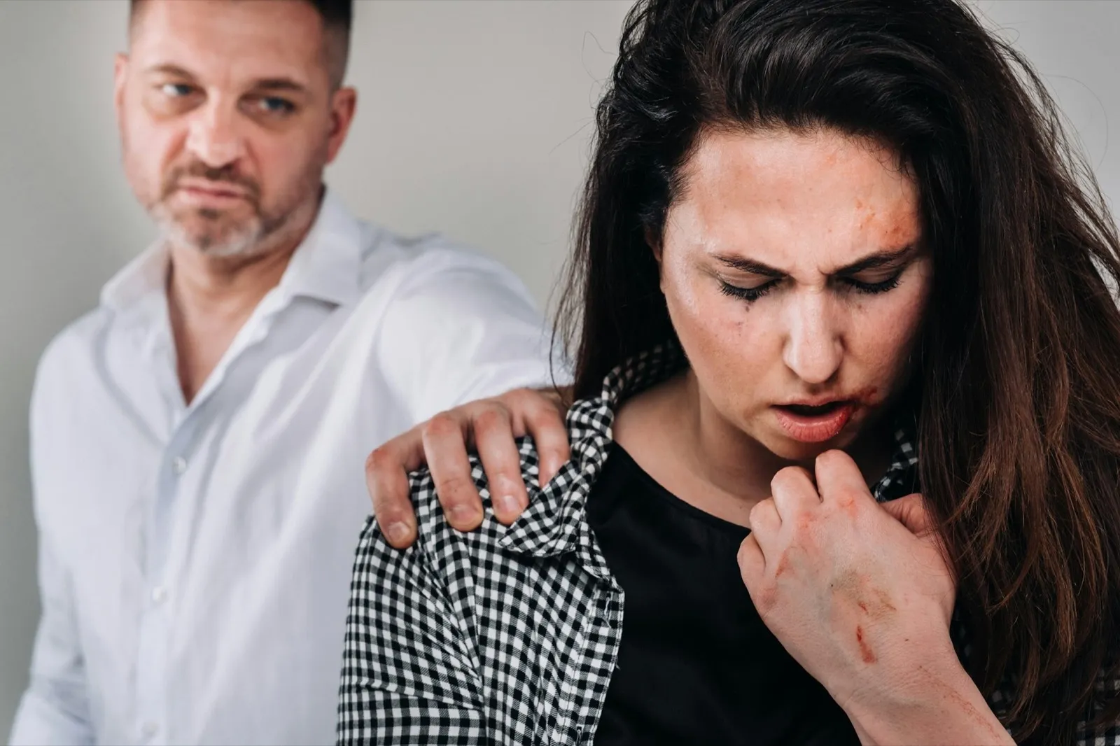 the male rapist put his hand on the shoulder of the beaten woman on a gray background. Domestic