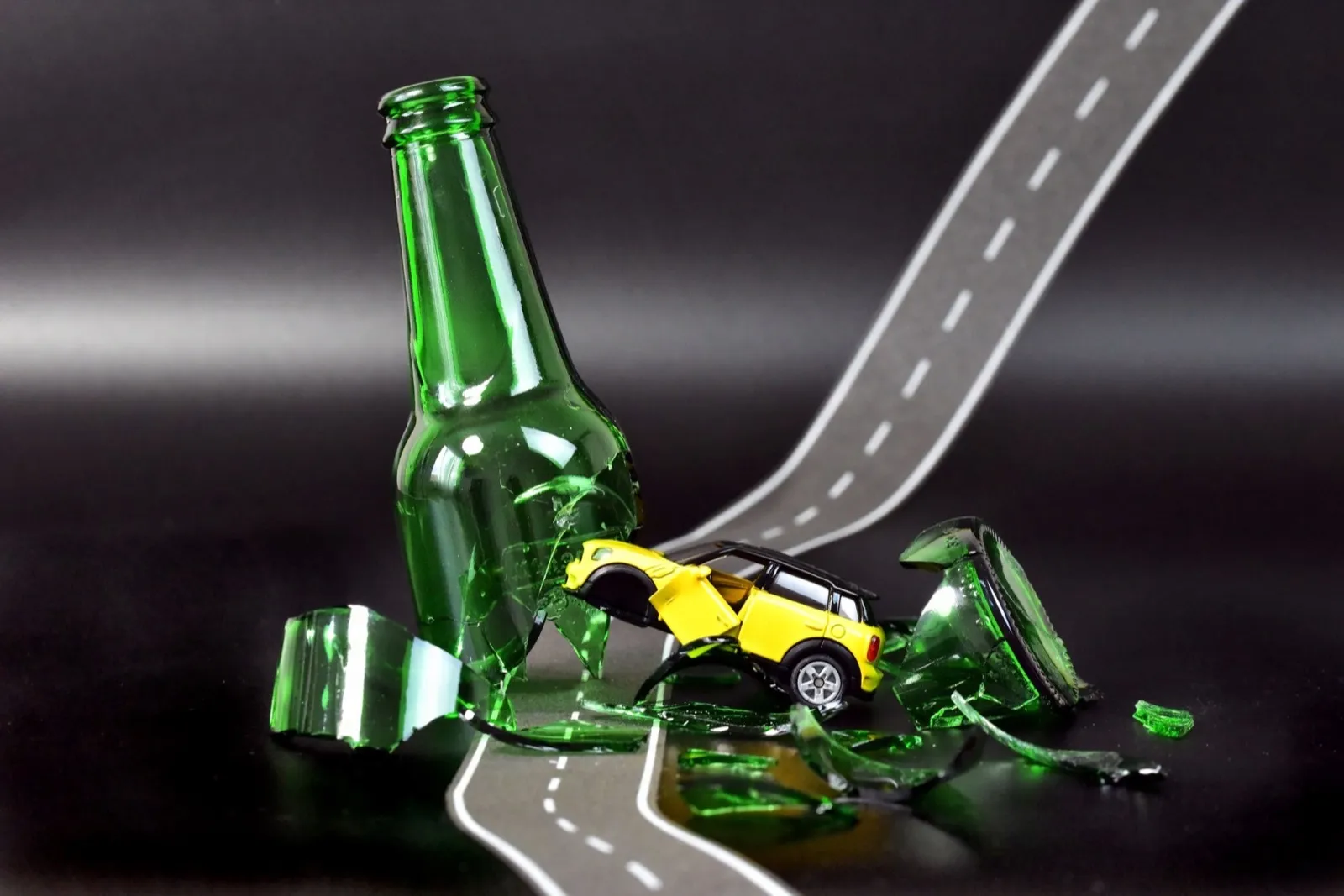 Toy car and a broken bottle with a road pattern surface - a concept of drunk driving